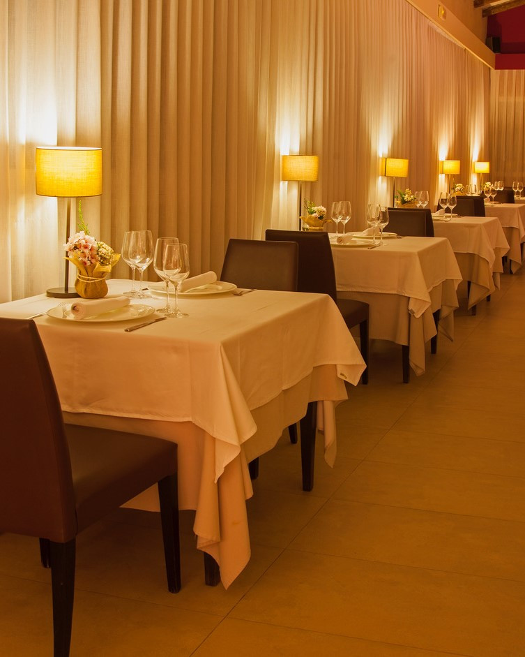 El comedor del Restaurante de Aldea Roqueta con mesas con mantel, lamparas de iluminación cálida, y platos y copas de vino. 